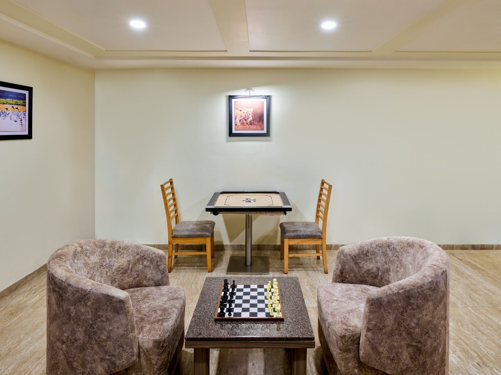 A room with a chessboard on a table, two chairs, and a framed picture on the wall.