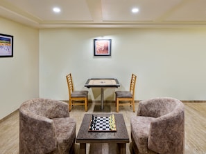 Quarto com um tabuleiro de xadrez sobre uma mesa, duas cadeiras e um quadro na parede.