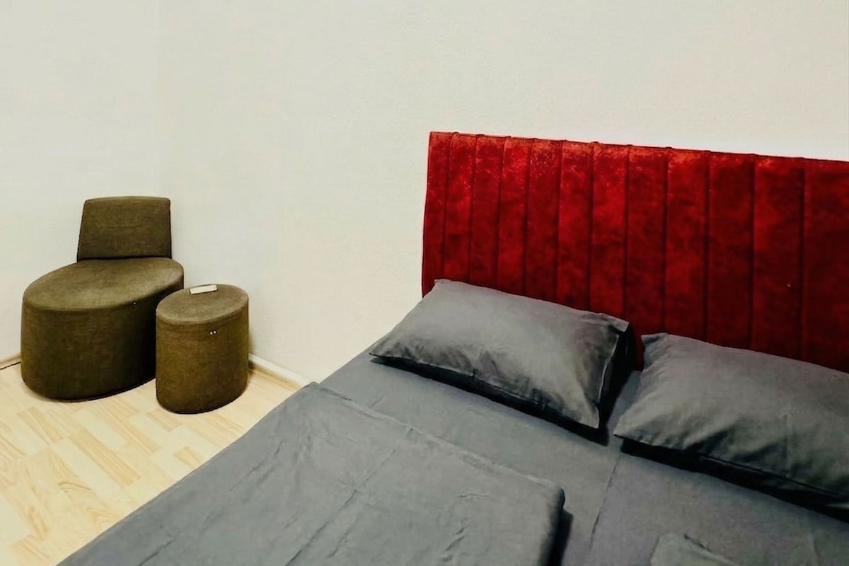 A bedroom with a bed, two ottomans, and a red headboard.