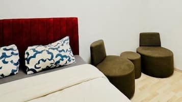 Een slaapkamer met een bed, twee kussens, een rood hoofdeinde en drie ronde stoelen.
