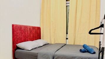 Una habitación pequeña con cama individual, cabecera roja, colchón gris y un par de jeans azules sobre la cama.