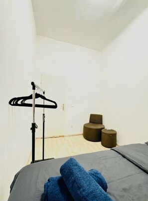 Una habitación con una cama, un perchero y dos taburetes redondos.