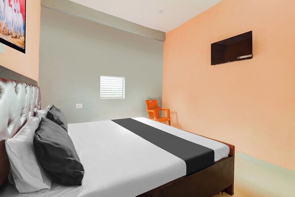 Quarto de hotel com cama, uma cadeira, janela e televisão fixada na parede.