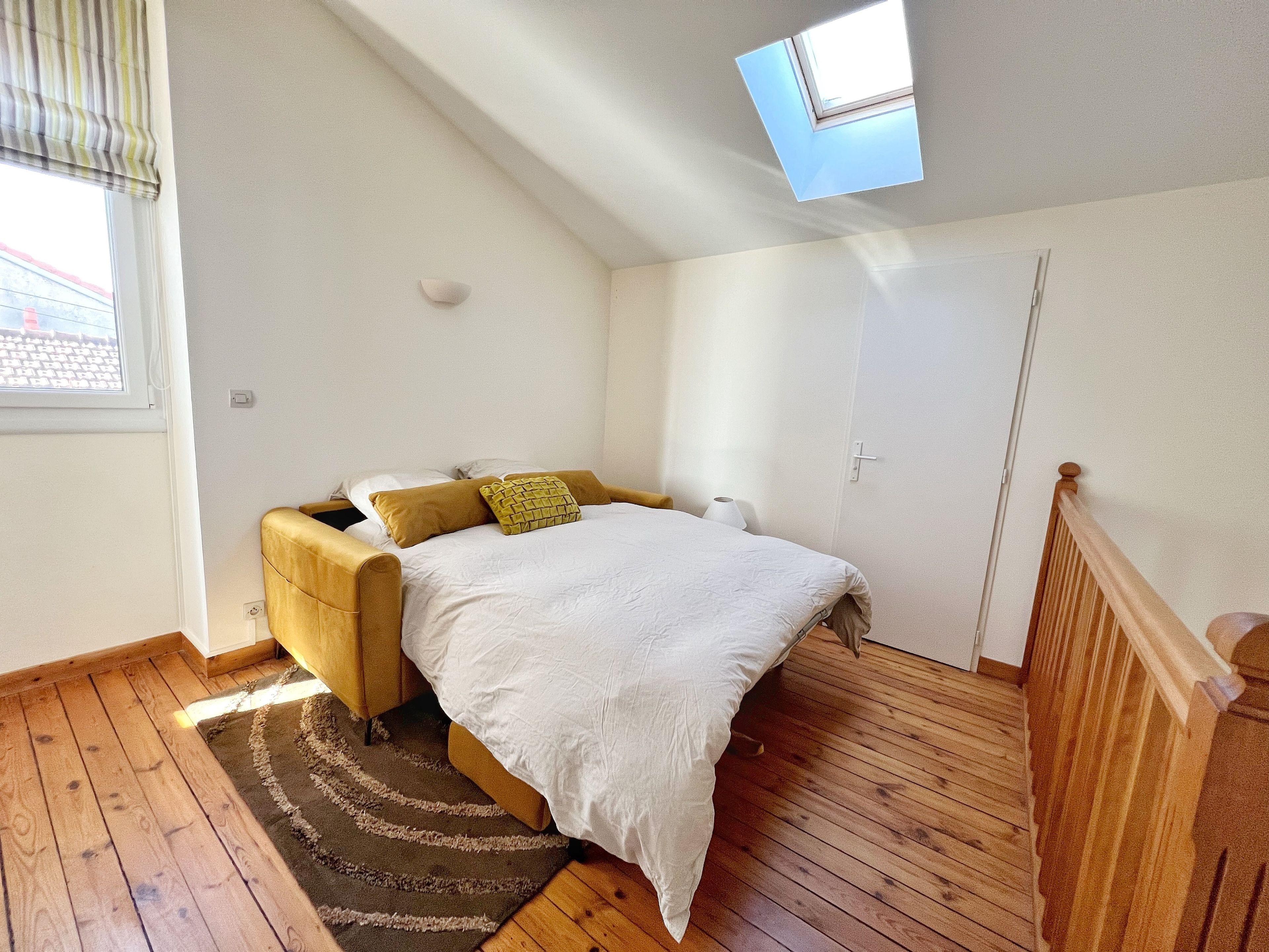 A bedroom with a bed, a window, a skylight, and a wooden floor.