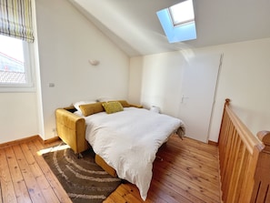 Une chambre à coucher avec un lit, une fenêtre, un puits de lumière et un plancher en bois.