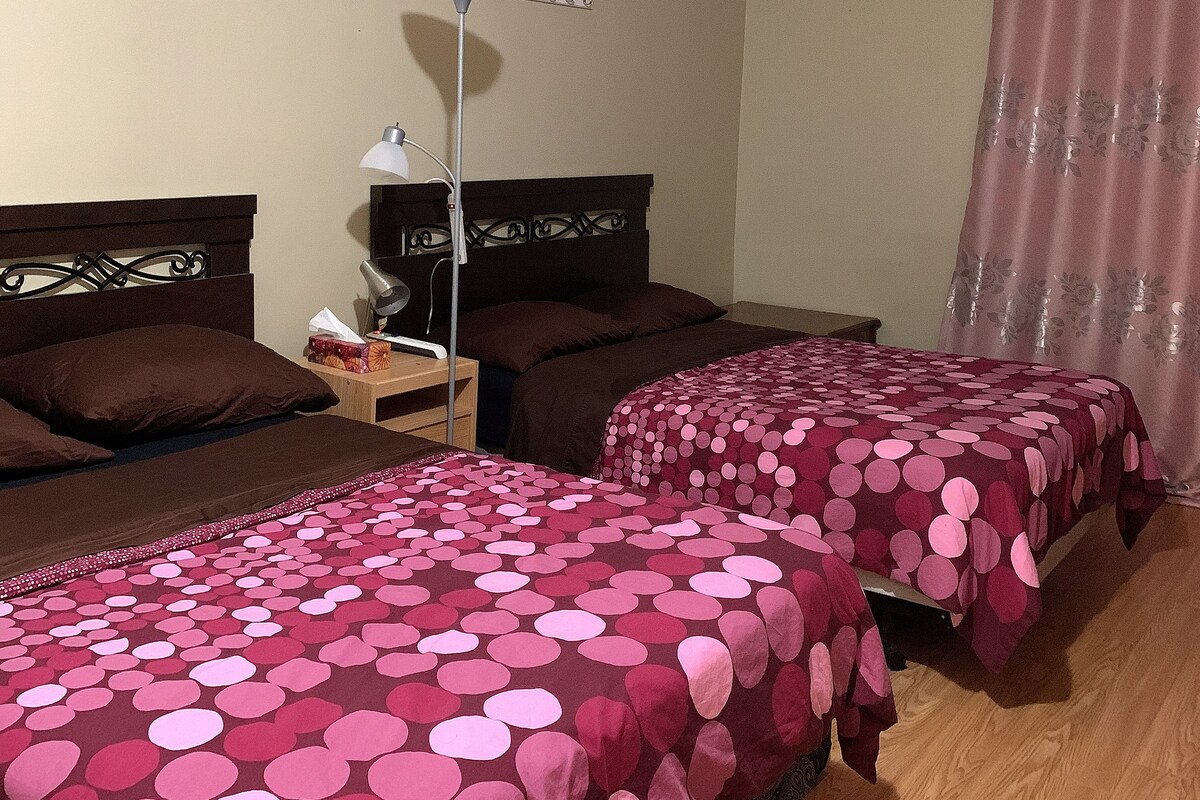 Une chambre d’hôtel avec deux lits, une table de chevet, une lampe, un rideau et un luminaire fixé au mur.