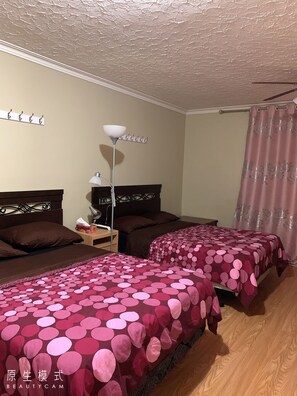 Une chambre d’hôtel avec deux lits, une table de chevet, une lampe, un rideau et un luminaire fixé au mur.