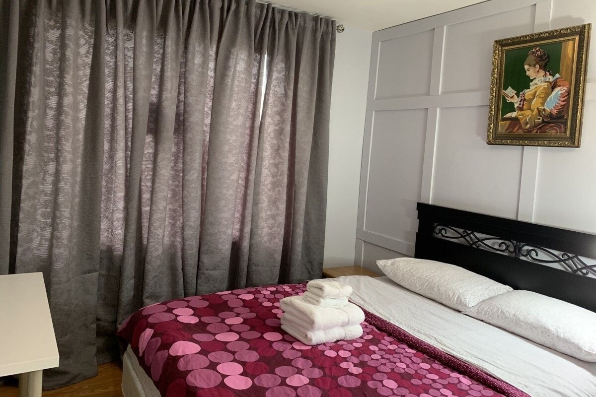 Une chambre d’hôtel avec un lit, des rideaux, un tableau et une lampe.