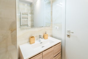 Un baño moderno con un lavamanos blanco, un mueble de madera y un espejo sobre el lavamanos.