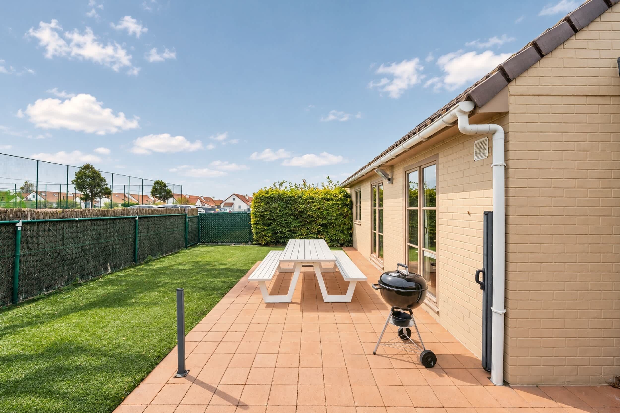 Un patio con una parrilla, una mesa de picnic y un jardín cercado.