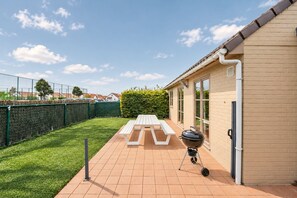 Eine Terrasse mit Grill, Picknicktisch und einem von einem Zaun umgebenen Garten.