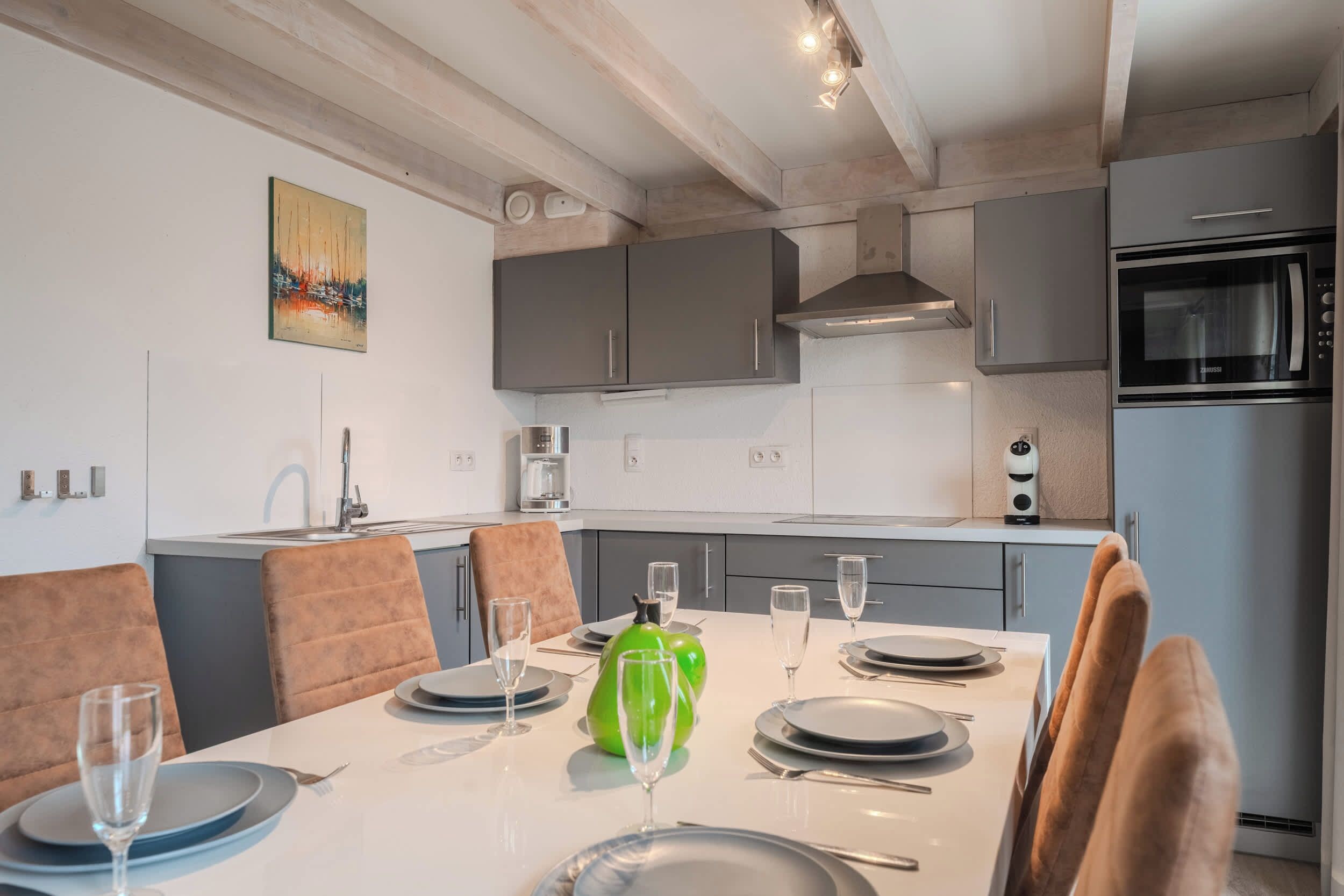 A modern kitchen with grey cabinets, a stainless steel oven, and a dining area with a white table set for four.