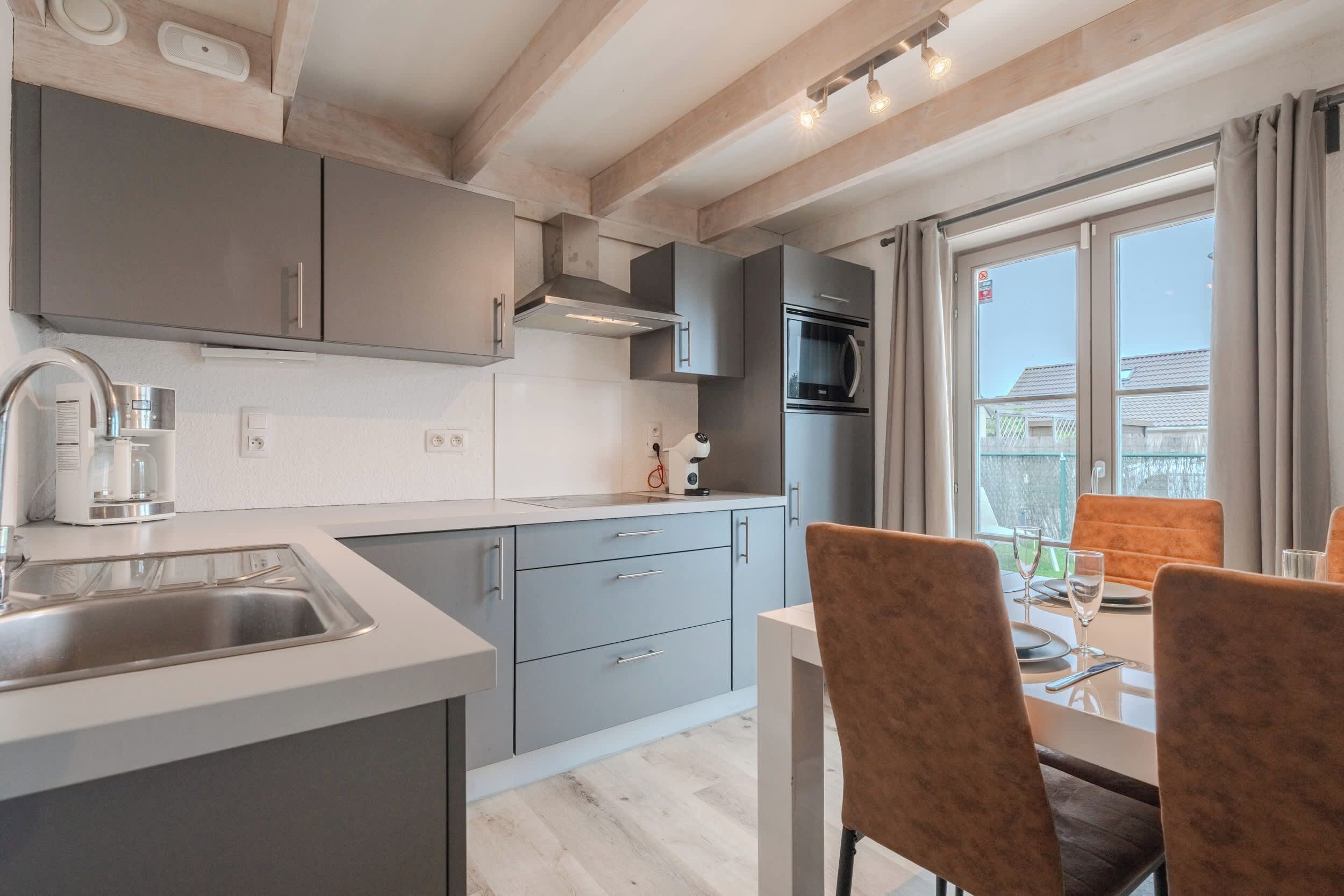 Une cuisine moderne avec des meubles gris, un évier en acier inoxydable et un coin repas comprenant une table et des chaises.
