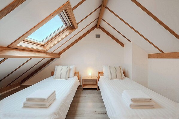 Une chambre avec deux lits, une lucarne et un plafond en pente.