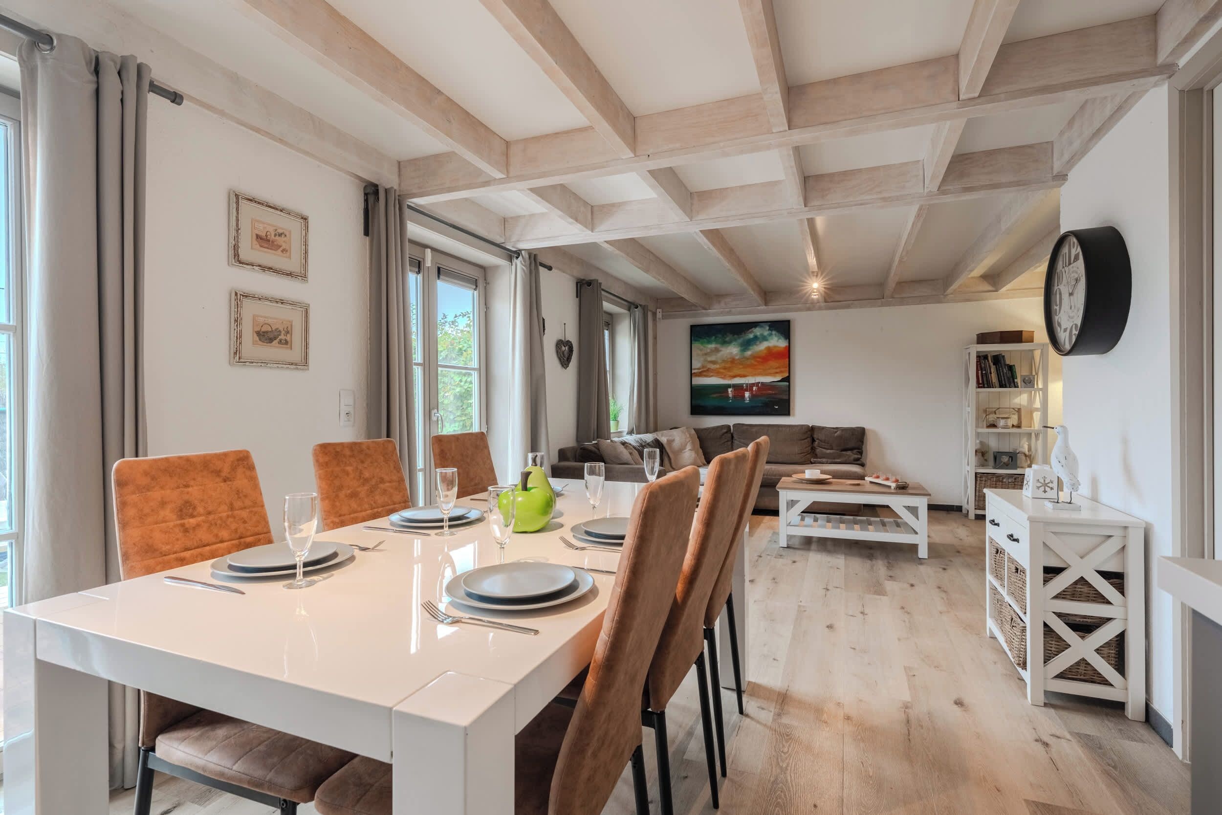 A dining area with a white table, brown chairs, and a painting on the wall.