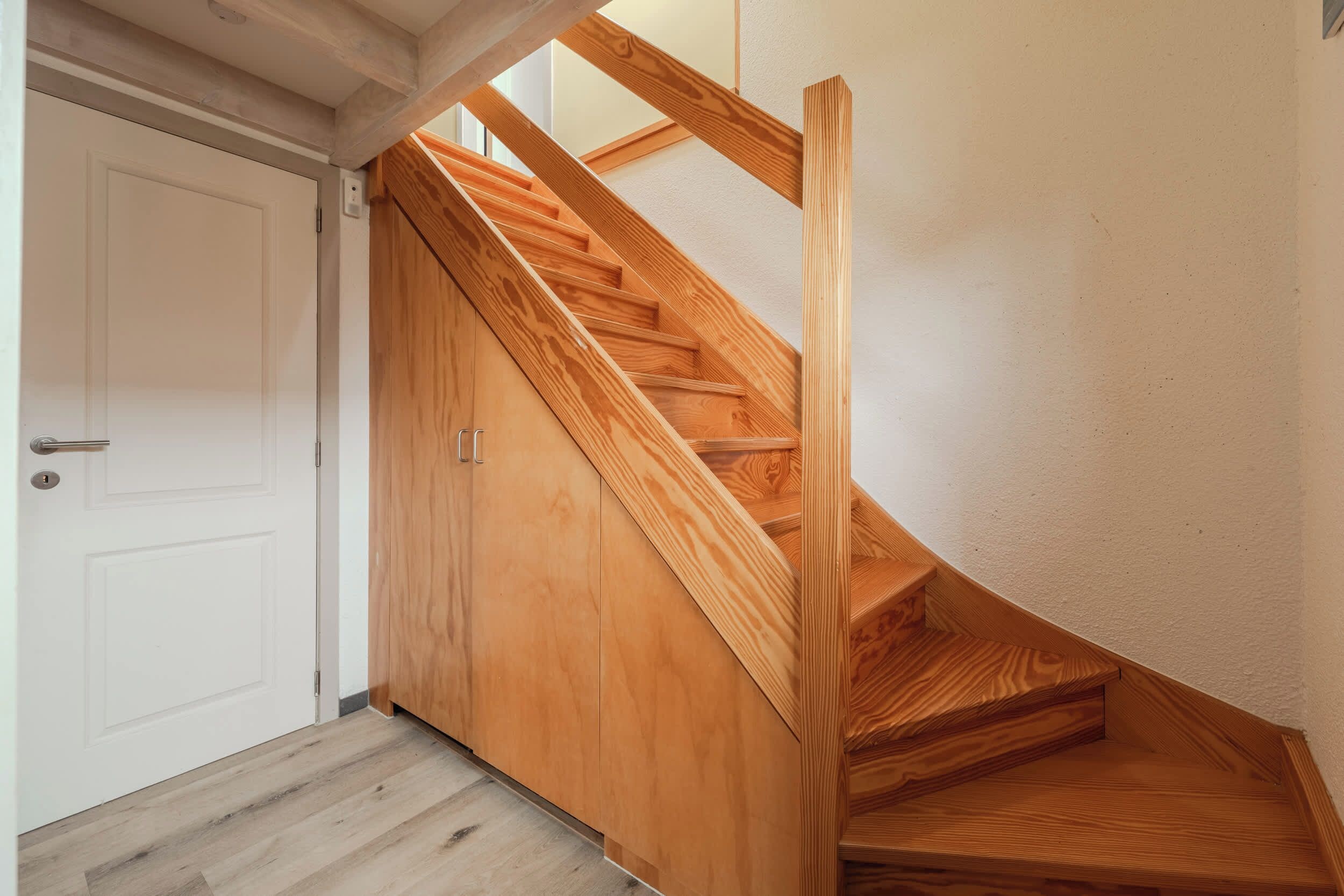 A wooden staircase with a white door and a light-colored wall.