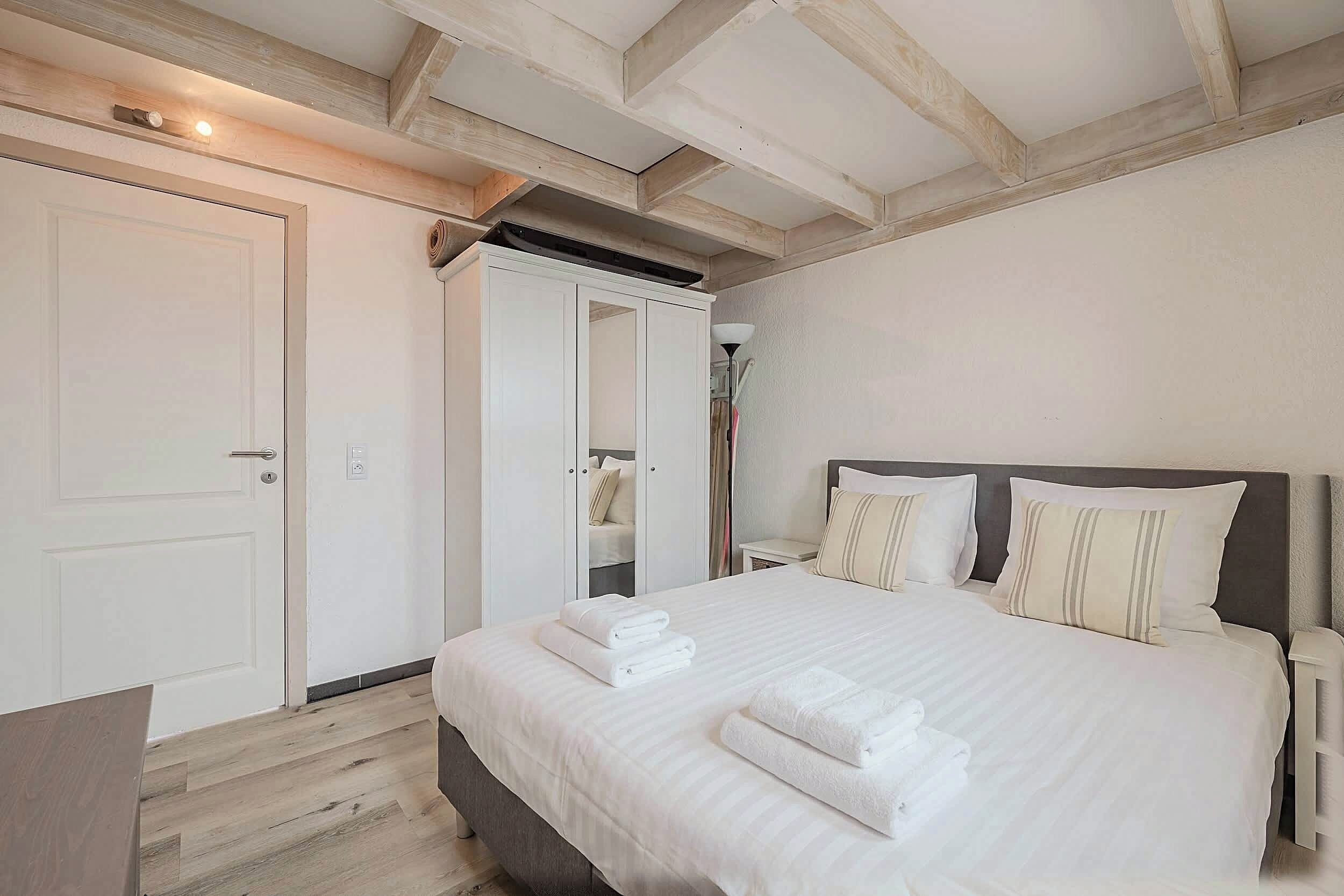 A bedroom with a large bed, a wardrobe, and a mirror.