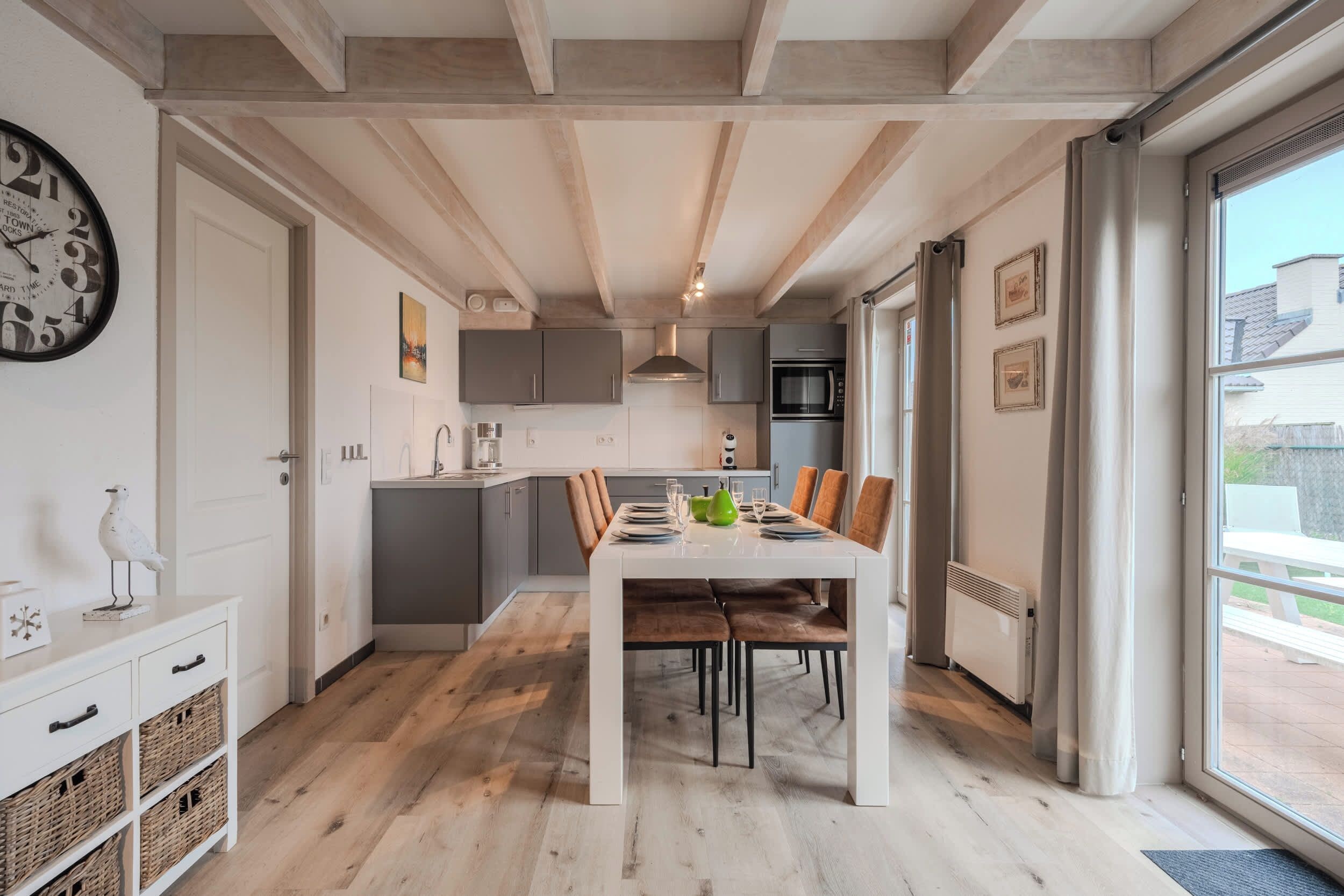 A modern kitchen with grey cabinets, a white countertop, and a dining area with a white table and brown chairs.