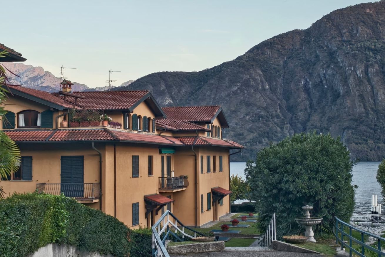Un bâtiment à deux étages, doté d’un toit recouvert de tuiles rouges, d’un balcon et offrant une vue sur un lac et des montagnes.