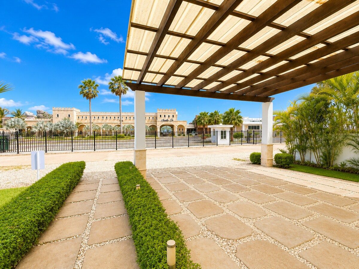 Un espacio al aire libre cubierto con un sendero pavimentado que conduce a un edificio con arcos y palmeras.