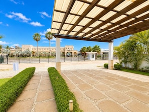 Un espacio al aire libre cubierto con un sendero pavimentado que conduce a un edificio con arcos y palmeras.