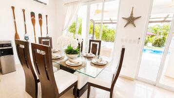 Un comedor moderno con una mesa de vidrio, sillas oscuras y vistas a una piscina.