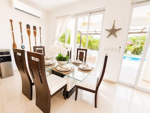 Un comedor moderno con una mesa de vidrio, sillas oscuras y vistas a una piscina.