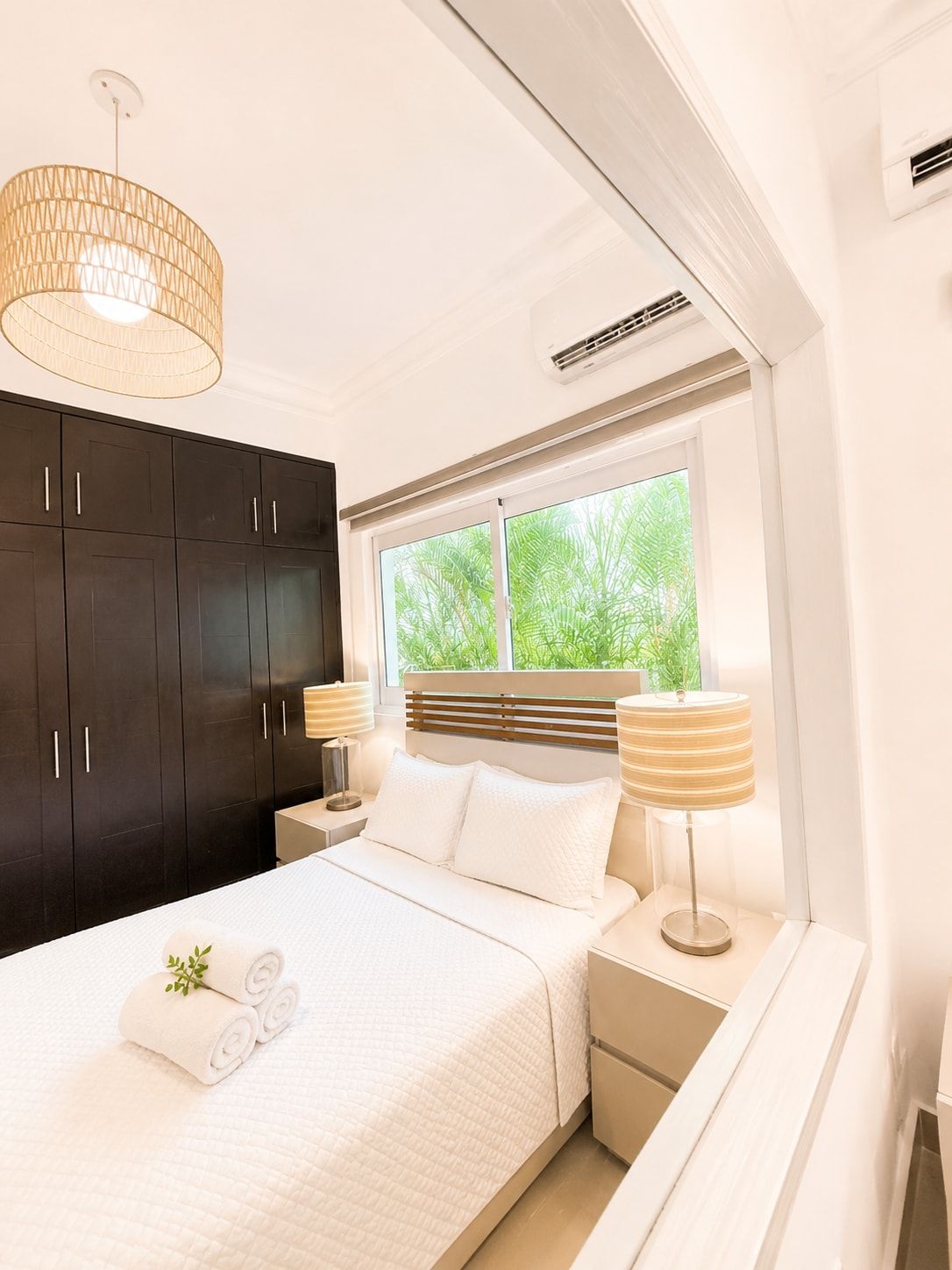 Un dormitorio moderno con cama, mesitas de noche, una ventana con vistas a zonas verdes y un armario oscuro.
