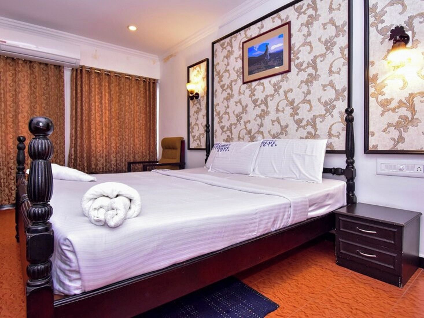 A hotel room with a large bed, a bedside table, a chair, and a wall-mounted lamp.