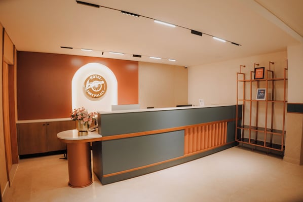 Una recepción de hotel con diseño moderno, un logotipo en la pared y una estantería metálica.