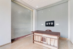 Un comptoir d’accueil avec un plateau en bois foncé et une étagère inférieure, une porte à volet enrouleur fermée et une enseigne murale portant le mot « OYO ».