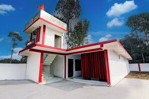 A hotel with a red and white facade, a staircase leading to the entrance, and a view of the surrounding trees. - Hotel O Alexa Hotel (Malihabad)