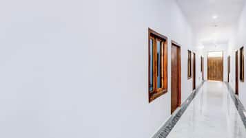 Un pasillo con paredes blancas, puertas de madera y suelo de mármol.