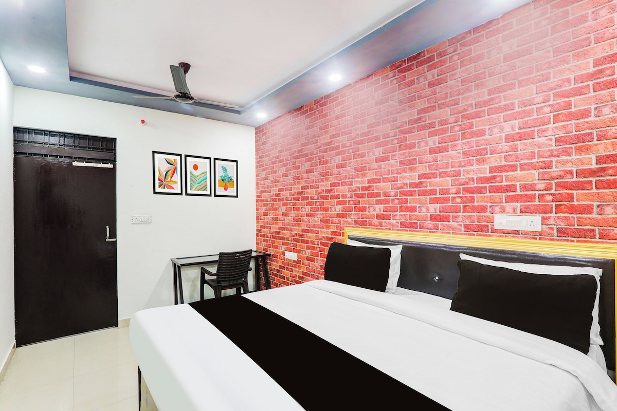 A hotel room with a brick wall, a bed with black and white bedding, a desk with a chair, and a ceiling fan.