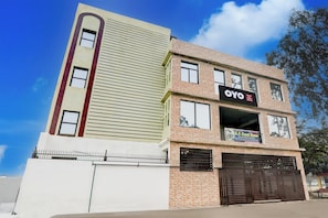 Un edificio de varios pisos con un llamativo rótulo de OYO Hotel, una entrada con portones y un cielo despejado.