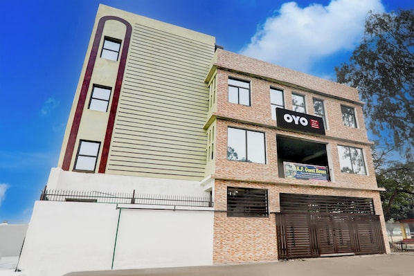 Un edificio de varios pisos con un llamativo rótulo de OYO Hotel, una entrada con portones y un cielo despejado.