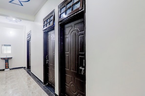 A hallway with two dark wooden doors, a white wall, and a small sink with a decorative design. - Hotel O Kp Guest House (Bara Banki)