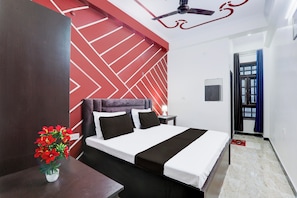 Habitación de hotel con cama, mesita de noche, lámpara, ventilador de techo y ventana con cortinas.