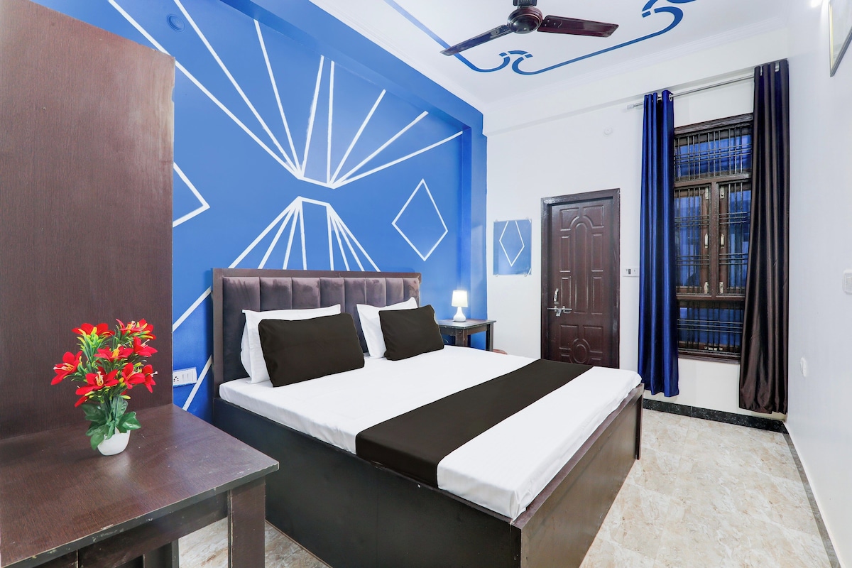 Habitación de hotel con cama, mesita de noche, lámpara, ventana con cortinas y puerta.
