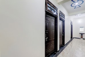 A hallway with dark wooden doors, a tiled floor, and a wall-mounted light fixture. - Hotel O Kp Guest House (Bara Banki)