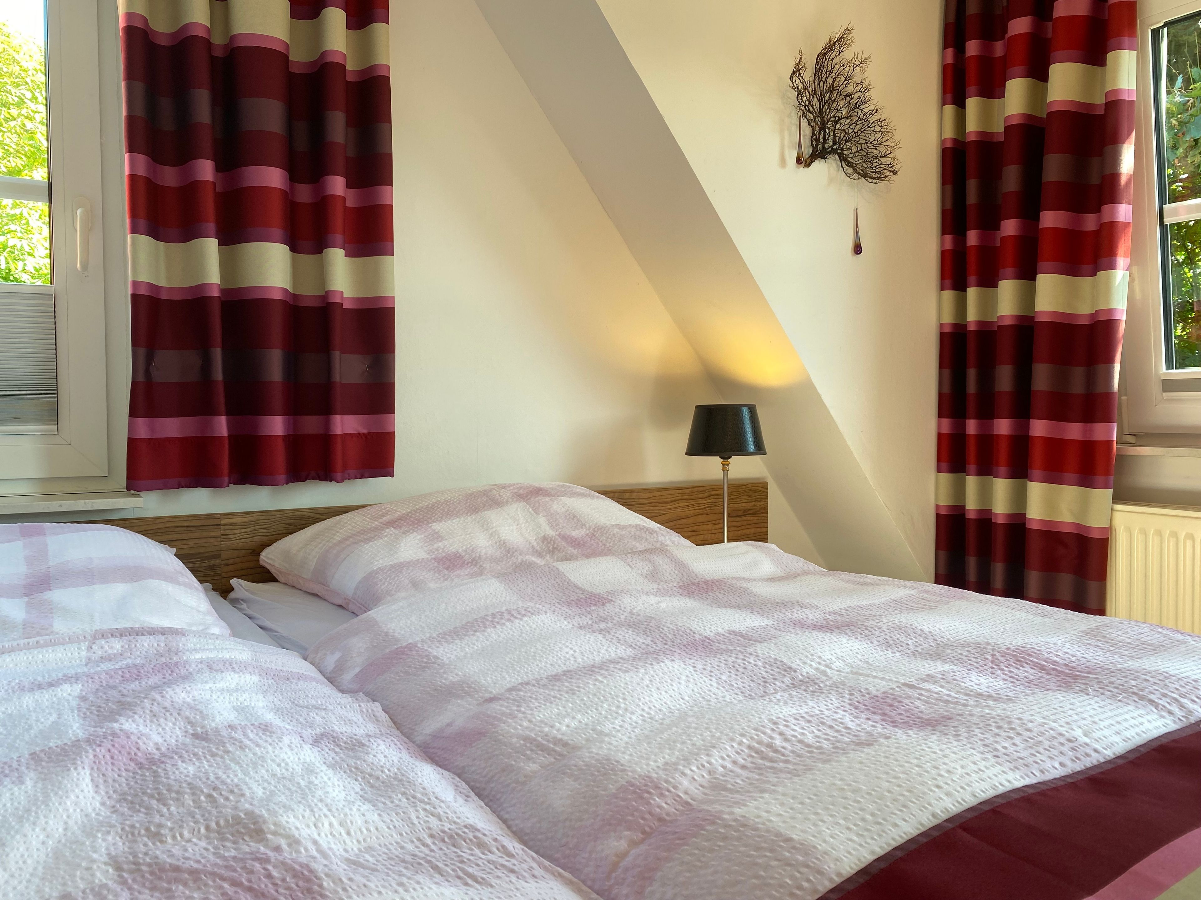 Ein Schlafzimmer mit zwei Betten, gestreifte Vorhänge, einer Wandlampe und einem Fenster mit Jalousien.