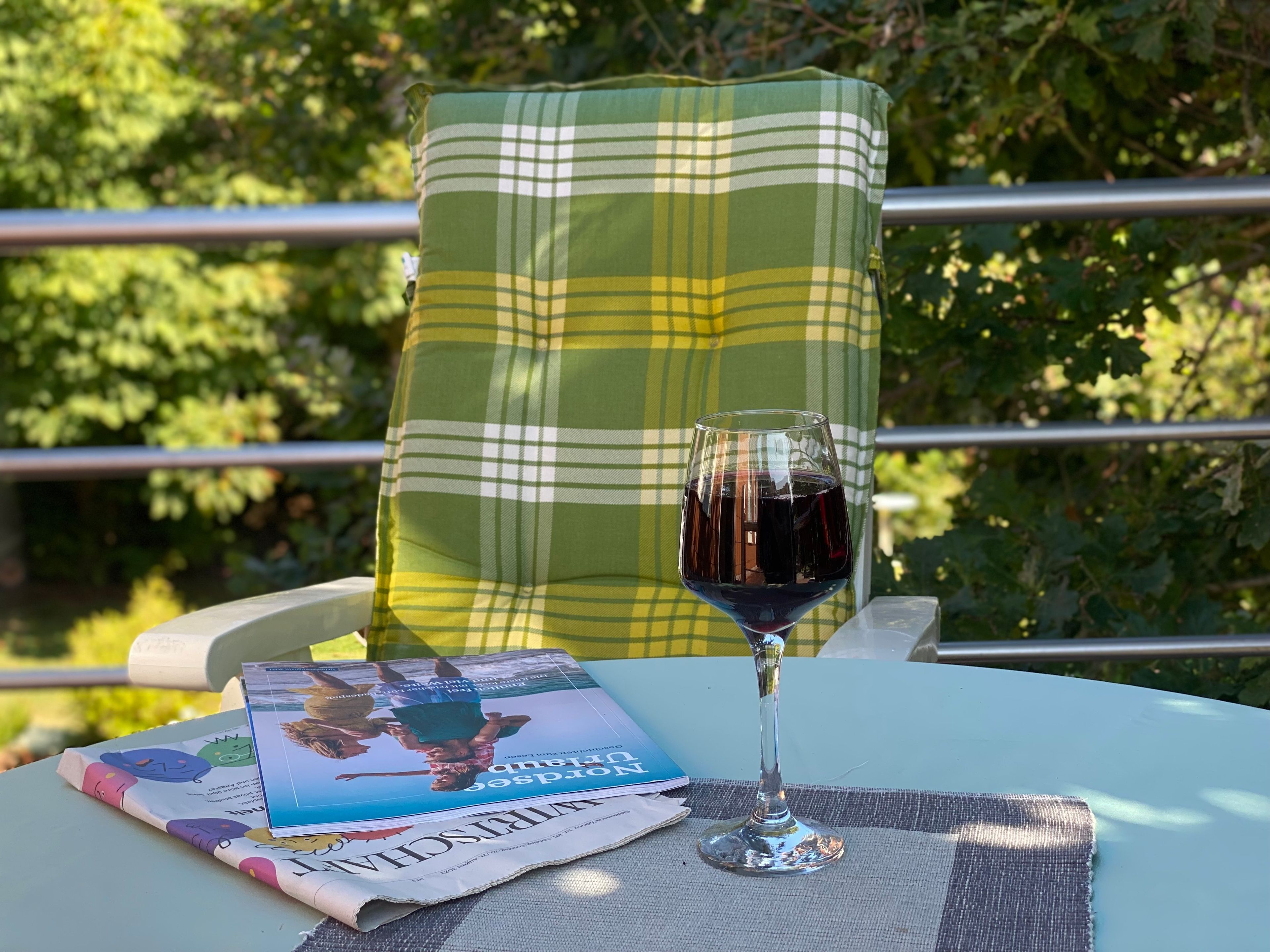Ein Glas Rotwein auf einem Tisch zusammen mit einer Zeitung und einer Zeitschrift.