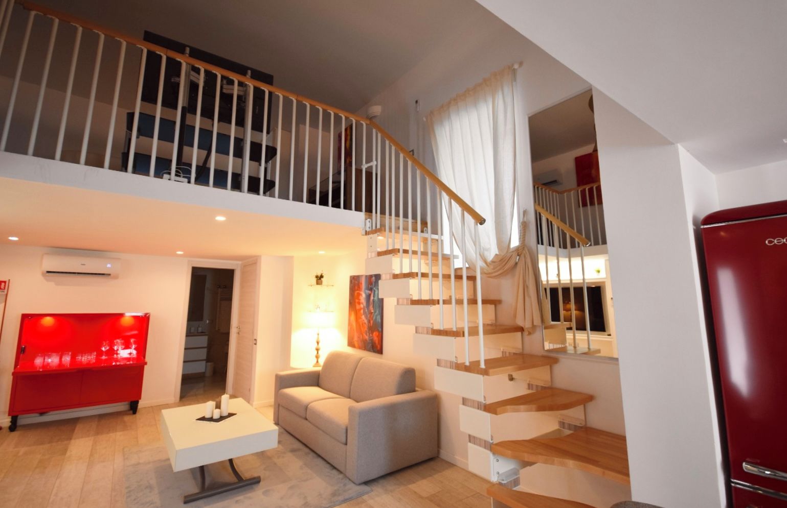 Un vaste espace de vie comprenant un escalier, un réfrigérateur rouge et un canapé moderne.