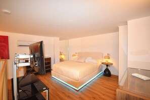 A modern hotel room with a bed, bedside lamps, a flat-screen TV, and a wooden floor. - New Listing (Cava de' Tirreni)