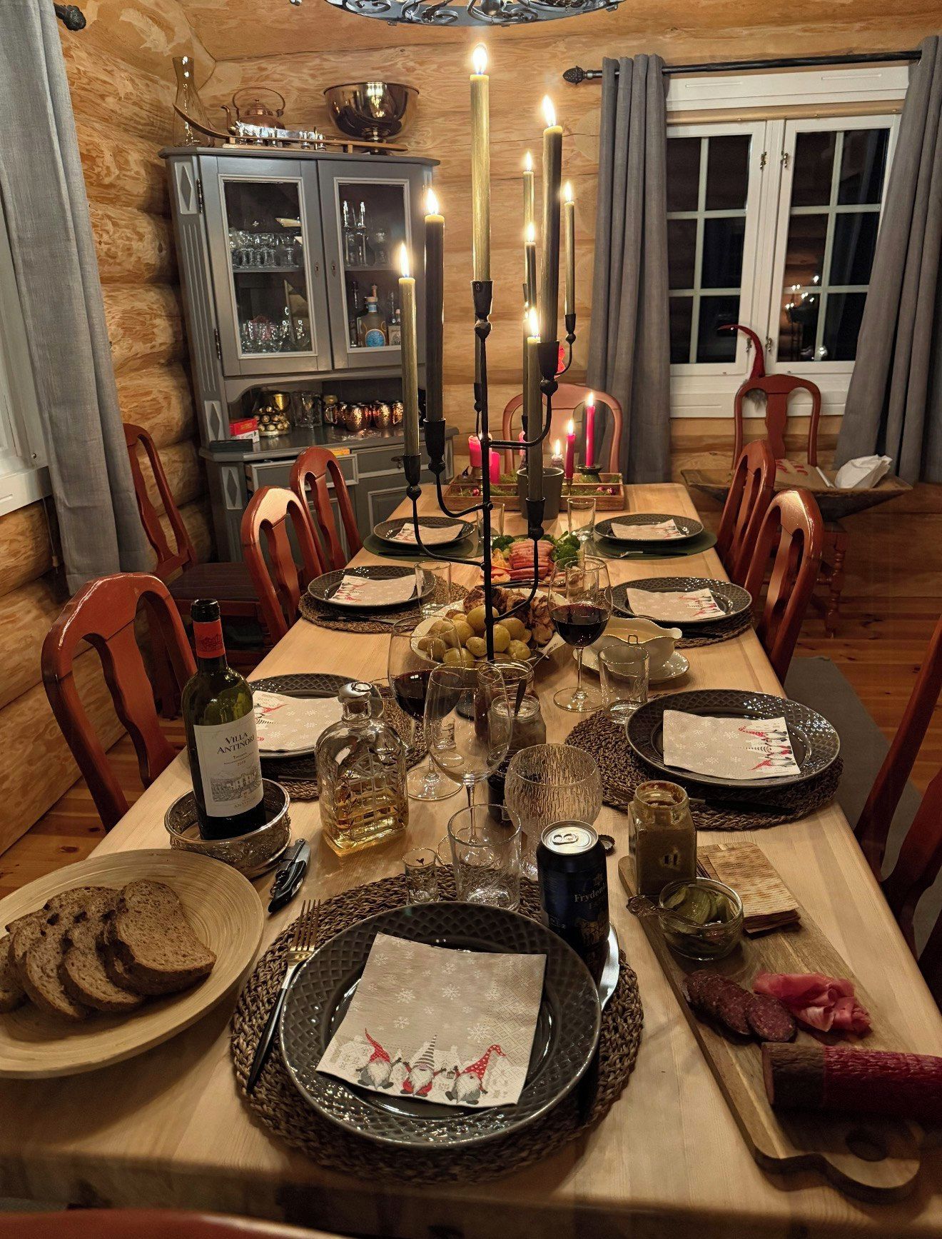 Comedor con una larga mesa dispuesta para una comida, con velas, platos, copas y una botella de vino.
