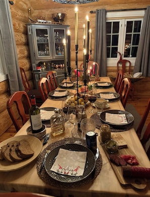 Comedor con una larga mesa dispuesta para una comida, con velas, platos, copas y una botella de vino.