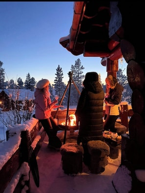 Eine Gruppe von Menschen versammelt sich um ein Lagerfeuer in einer verschneiten Outdoor-Umgebung.