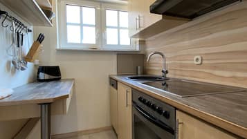 A compact kitchen with a stove, oven, sink, and window.