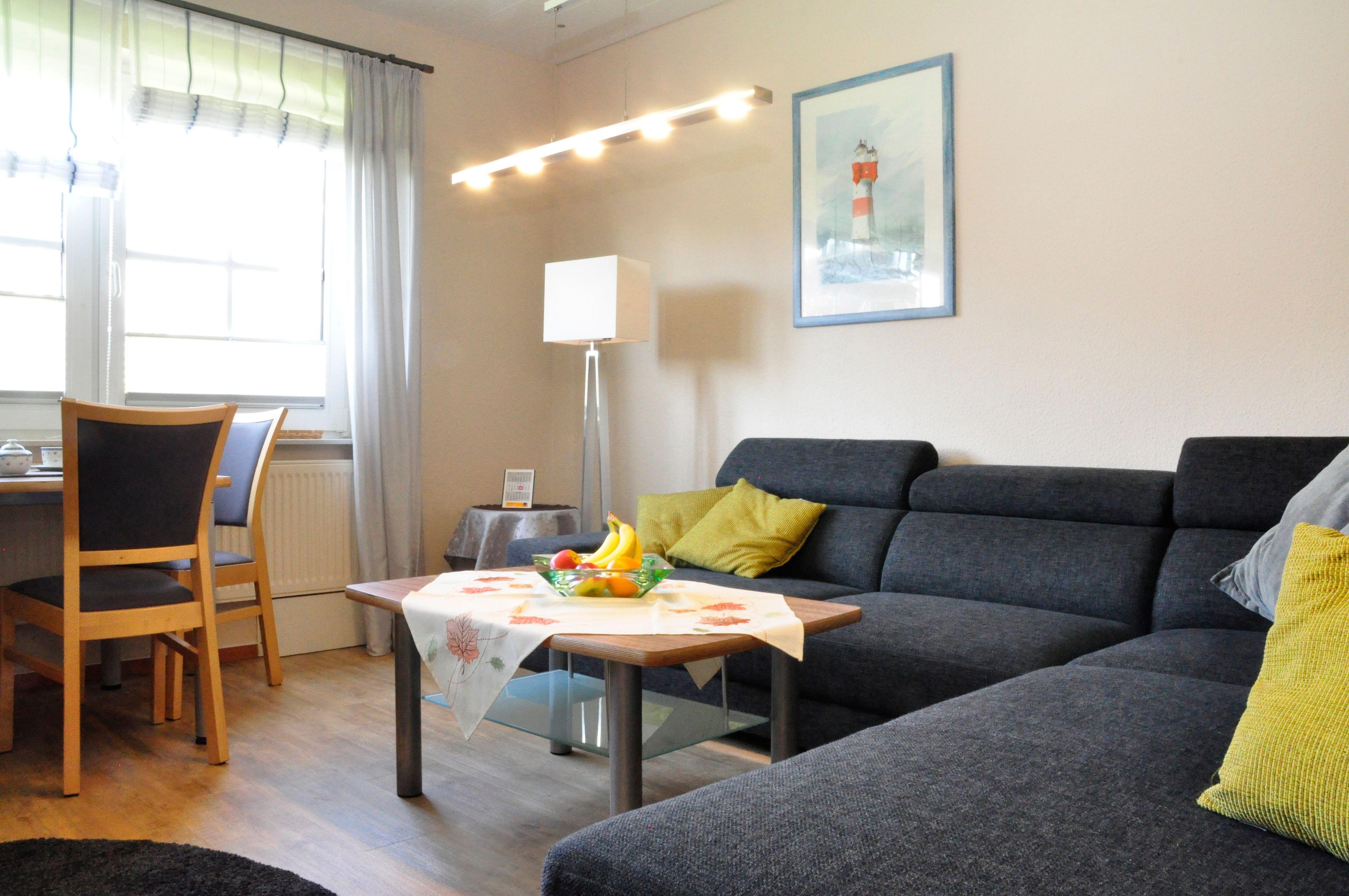 A living room with a sofa, a dining table with chairs, a lamp, and a framed picture on the wall.