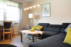Ein Wohnzimmer mit einer Couch, einem Esstisch mit Stühlen, einer Lampe und einem gerahmten Bild an der Wand.
